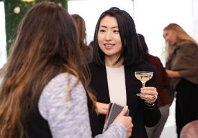 Woman holding drink connecting with another during International Women's Day Event.